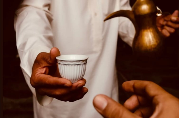 Saudi man offering a small cup of Saudi coffee